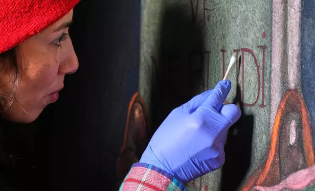 Art conservator Naomi Ruiz uses a cotton swab on a mural by Maxo Vanka that depicts the hand of God handing a tablet to Moses, inside St. Nicholas Croatian Catholic Church in Millvale, Pa., Wednesday, Feb. 19, 2025. (AP Photo/Gene J. Puskar)