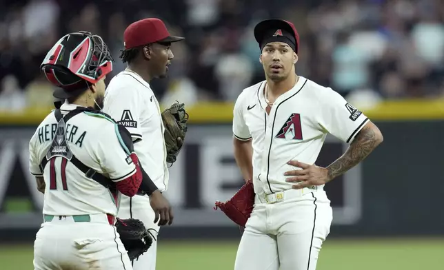 Arizona Diamondbacks pitcher Justin Martinez, right, pauses on the pitcher's mound after an injury as Diamondbacks catcher Jose Herrera, left, and Diamondbacks shortstop Geraldo Perdomo check on Martinez during the ninth inning of a baseball game against the Seattle Mariners Monday, June 9, 2025, in Phoenix. (AP Photo/Ross D. Franklin)