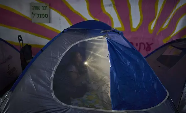 A person illuminates a light inside a tent while spending the night in a public shelter as a precaution against possible Iranian missile attacks, in Tel Aviv, Israel, Saturday, June 21, 2025. (AP Photo/Ohad Zwigenberg)