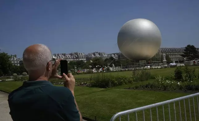 A man takes a snapshot of the Olympic cauldron at the Tuileries Gardens, ahead of its nightly summer relaunch starting June 21, in Paris, Thursday, June 12, 2025. (AP Photo/Michel Euler)