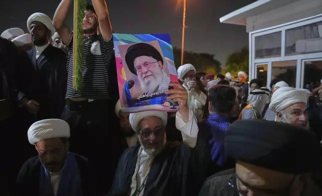 An Iraqi Shiite cleric holds a portrait of Iran's Supreme Leader Ayatollah Ali Khamenei during a protest against Israeli attacks on multiple cities across Iran, at a bridge leading to the fortified Green Zone where the U.S. Embassy is located in Baghdad, Iraq, Thursday, June 19, 2025. (AP Photo/Hadi Mizban)