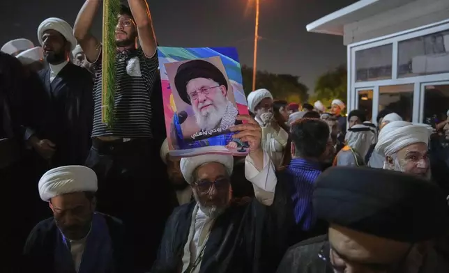 An Iraqi Shiite cleric holds a portrait of Iran's Supreme Leader Ayatollah Ali Khamenei during a protest against Israeli attacks on multiple cities across Iran, at a bridge leading to the fortified Green Zone where the U.S. Embassy is located in Baghdad, Iraq, Thursday, June 19, 2025. (AP Photo/Hadi Mizban)