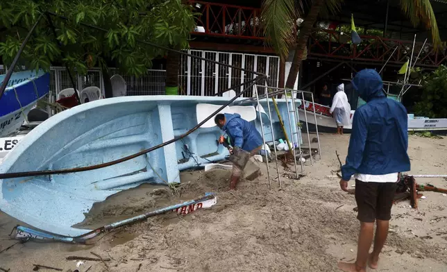 A person removes sand from a boat that was taken offshore in preparation for Hurricane Erick after the storm hit near Puerto Escondido, Oaxaca state, Mexico, Thursday, June 19, 2025. (AP Photo/Luis Alberto Cruz)