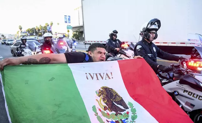 Roberto Alvarez waves a Mexican flag as police officers move protesters out of a street Friday, June 13, 2025, in Los Angeles. (AP Photo/Noah Berger)