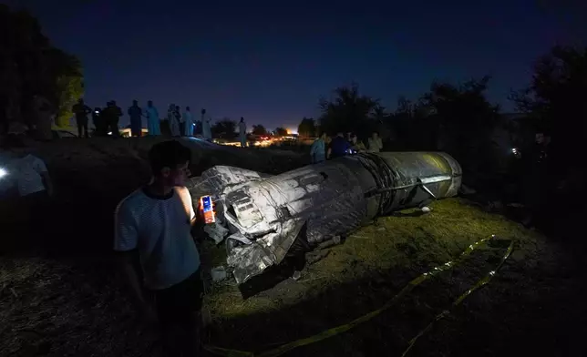 People view remnants of a missile fallen on a field between Najaf and Karbala, Iraq, Friday, June 13, 2025. (AP Photo/Anmar Khalil)