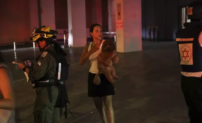A woman holds her dog next to a building struck by a missile fired from Iran, in Tel Aviv, Israel, on Friday, June 13, 2025. (AP Photo/Tomer Appelbaum)