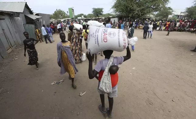 Refugees carry food at a distribution center run by the World Food Programme (WFP) at Kakuma Refugee Camp in Turkana, Kenya Tuesday, June 3, 2025. (AP Photo/Andrew)