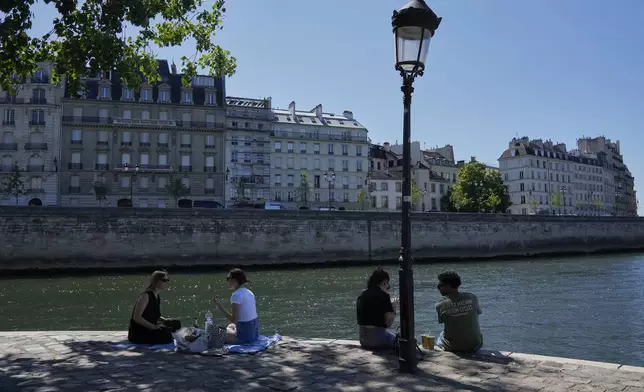 People sit in the shade along the Seine river in Paris, Sunday, June 29, 2025. (AP Photo/Michel Euler)