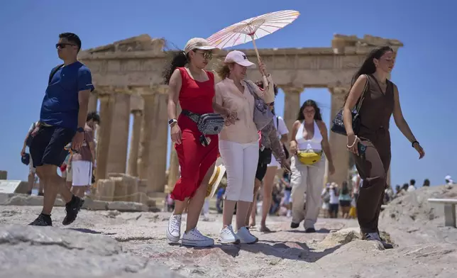 Tourists with an umbrella walk in front of the ancient Parthenon temple at the Acropolis Hill, Thursday, June 26, 2025, as the summer's first heat wave hits Greece, with temperatures expected to edge over 40 degrees Celsius, (104 Farenheit).(AP Photo/Petros Giannakouris)