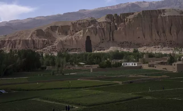 FILE.- Villagers walk in the fields near the niche of the giant Buddha statue destroyed by the Taliban in 2001, in Bamiyan, Afghanistan, Saturday, June 17, 2023. (AP Photo/Rodrigo Abd,File