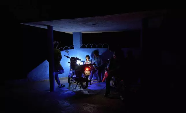 People wait at a bus stop lit by a motorcycle's headlights during a partial power outage in La Gallega, Havana province, Cuba, Sunday, June 1, 2025. (AP Photo/Ramon Espinosa)