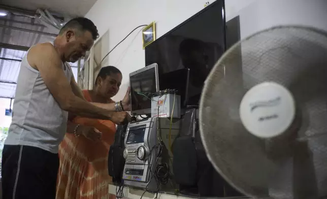 Married couple Angel Rodriguez and Marylin Alvarez set up a motorcycle battery to power a laptop screen to watch television, as they stay prepared for blackouts in the Bahia neighborhood of Havana, Cuba, Monday, May 26, 2025. (AP Photo/Ramon Espinosa)