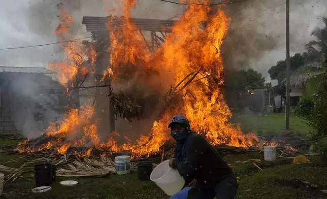 Residents try to extinguish a burning hut during clashes between anti-government protesters and police in the Indigenous Embera community of Arimae, Panama, Thursday, June 5, 2025.(AP Photo/Matias Delacroix)