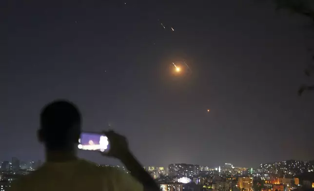 A man takes a cellphone photo as missiles fired from Iran toward Israel fly over Syrian territory in Damascus, Syria, early Wednesday, June 18, 2025. (AP Photo/Ghaith Alsayed)
