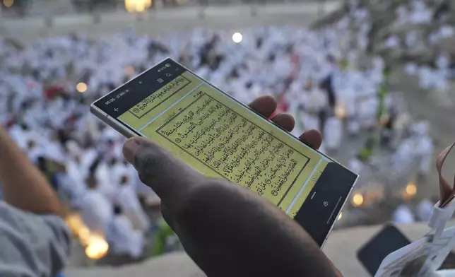A Muslim pilgrim uses a mobile phone to read chapters from the holy Quran atop the rocky hill known as the Mountain of Mercy, on the Plain of Arafat, during the annual Hajj pilgrimage near the holy city of Mecca, Saudi Arabia, Thursday, June 5, 2025. (AP Photo/Amr Nabil)