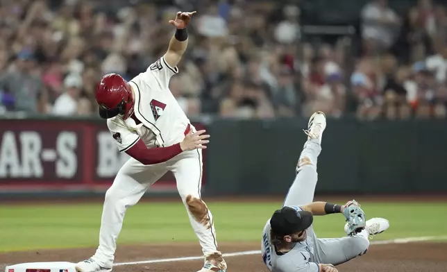 Arizona Diamondbacks' Randal Grichuk, left, slides safely into third base as Miami Marlins third baseman Connor Norby dives to make a catch on a throw from the outfield during the fourth inning of a baseball game Saturday, June 28, 2025, in Phoenix. (AP Photo/Ross D. Franklin)