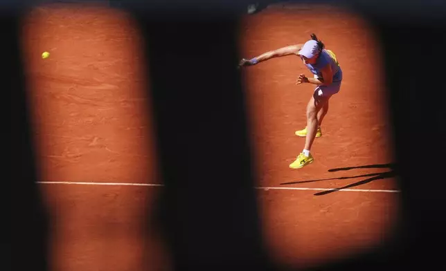Poland's Iga Swiatek is seen through a fence as she serves against Romania's Jaqueline Cristian during their third round match of the French Tennis Open, at the Roland-Garros stadium, in Paris, Friday, May 30, 2025. (AP Photo/Lindsey Wasson)