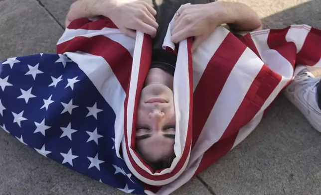 A demonstrator wraps themselves with a U.S. flag during a protest outside Dodger Stadium Saturday, June 21, 2025, in Los Angeles. (AP Photo/Damian Dovarganes)