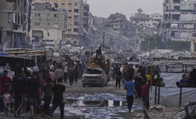 A damaged car carrying furniture and a mattress drives among pedestrians through a market surrounded by destroyed buildings in Gaza City, northern Gaza Strip, on Sunday, June 22, 2025. (AP Photo/Jehad Alshrafi)