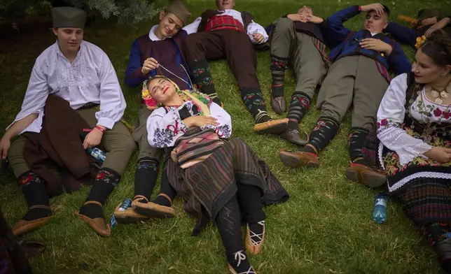 Members of a traditionial group from Serbia rest in the shade before a parade by international ensembles and those of ethnic groups from Romania showcasing traditional outfits, dances and songs, in Bucharest, Romania, Saturday, June 21, 2025. (AP Photo/Vadim Ghirda)