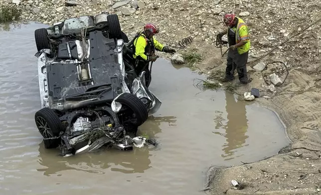 A crew works near a vehicle that was swept away in floodwaters in San Antonio, Texas, on Thursday, June 12, 2025. (AP Photo/Lekan Oyekanmi)