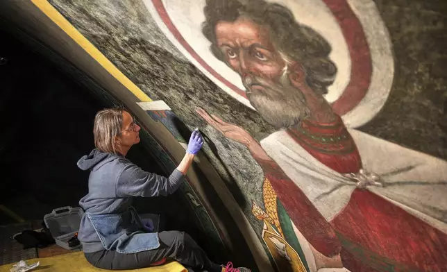 Sitting on a 32-foot-tall scaffold, art conservator Cricket Harbeck works on cleaning a mural by Maxo Vanka depicting St. Mark, inside St. Nicholas Croatian Catholic Church in Millvale, Pa., Monday, May 19, 2025. (AP Photo/Gene J. Puskar)
