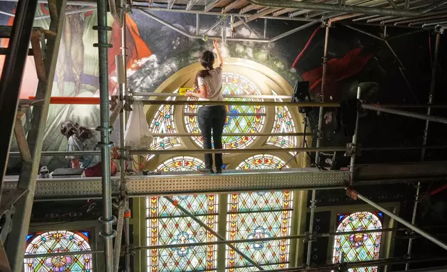 Standing on a 32-foot-tall scaffold, conservation technician Celeste Parrendo works on touching up a mural by Maxo Vanka inside St. Nicholas Croatian Catholic Church in Millvale, Pa., Monday, May 19, 2025. (AP Photo/Gene J. Puskar)