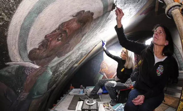 Art conservation technician Celeste Parrendo, right, works on a mural by Maxo Vanka that depicts St. Matthew, inside St. Nicholas Croatian Catholic Church in Millvale, Pa., Feb 13, 2025. (AP Photo/Gene J. Puskar