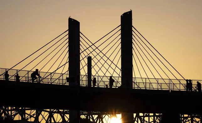 Poeple walk across the Big Four Bridge as the sun sets at Waterfront Park on Sunday, June 22, 2025, in Louisville, Ky. (AP Photo/Jon Cherry)