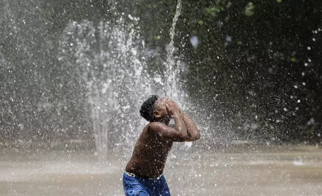 A child covers his face while a stream of water pours down at Waterfront Park on Sunday, June 22, 2025, in Louisville, Ky. (AP Photo/Jon Cherry)
