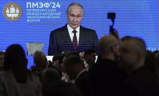 Guests and participants walk in front of a TV screen showing Russian President Vladimir Putin on the sidelines of the St. Petersburg International Economic Forum in St. Petersburg, Russia, Wednesday, June 18, 2025. (AP Photo/Dmitri Lovetsky)