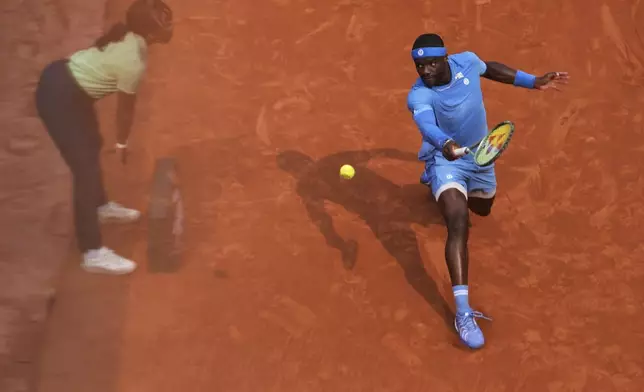 A referee is reflected in a glass as Frances Tiafoe of the U.S. plays a shot against Italy's Lorenzo Musetti during their quarterfinal match of the French Tennis Open at the Roland-Garros stadium in Paris, Tuesday, June 3, 2025. (AP Photo/Thibault Camus)