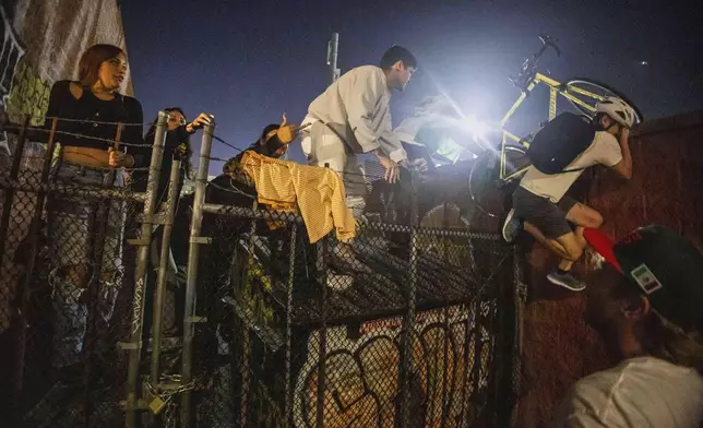 Protesters jump over a fence to avoid being kettled by police during protests over the Trump administration's immigration raids in Los Angeles, Monday, June 9, 2025. (AP Photo/Ethan Swope)