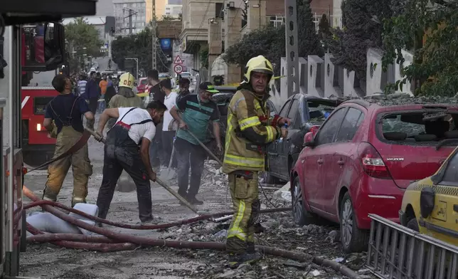 Firefighters and people clean up the scene of an explosion at a residence compound after Israeli attacks in Tehran, Friday, June 13, 2025. (AP Photo/Vahid Salemi)