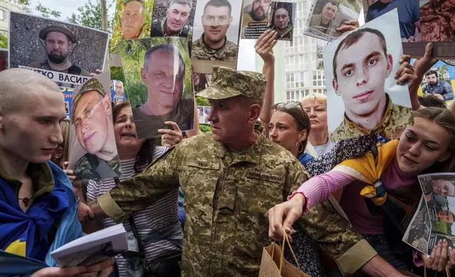 An Ukrainian soldier, left, walks though human corridor with people holding photos of their missed relatives after returning from captivity after a POWs exchange between Russia and Ukraine, in Chernyhiv region, Ukraine, Monday, June 9, 2025. (AP Photo/Evgeniy Maloletka)