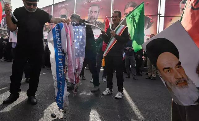People burn the representations of the U.S. and Israeli flags as a poster of the late Iranian revolutionary founder Ayatollah Khomeini is held at right during the funeral ceremony of Iranian armed forces generals, nuclear scientists and their family members killed in a 12-day war with Israel, in Tehran, Iran, Saturday, June 28, 2025. (AP Photo/Vahid Salemi)