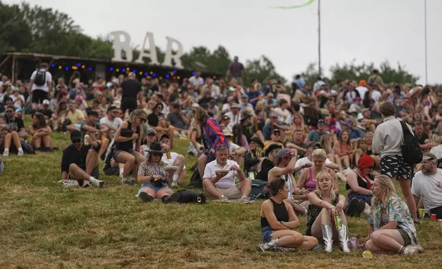 Festivalgoers sit outside a bar during the Glastonbury Festival in Worthy Farm, Somerset, England, Wednesday, June 25, 2025. (Scott A Garfitt/Invision/AP)