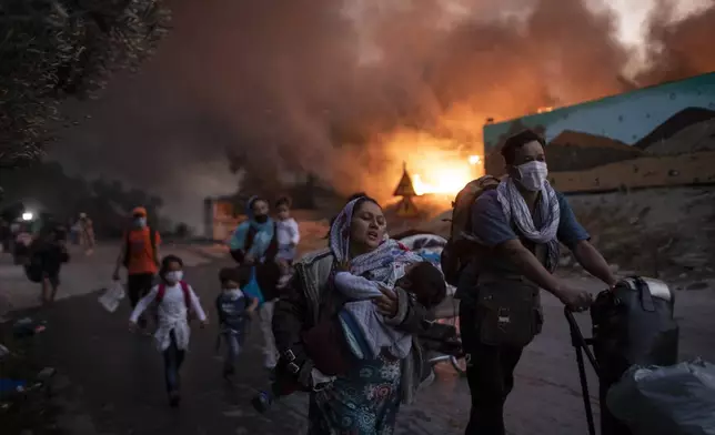 FILE - Refugees and migrants carrying children and belongings flee a fire burning at the Moria camp on the northeastern Aegean island of Lesbos, Greece on Wednesday, Sept. 9, 2020. (AP Photo/Petros Giannakouris, File)