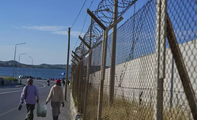 Refugees walk next to a fence with razor wire outside the Kara Tepe refugee and migrant camp on the island of Lesbos, Greece, May 13, 2025. (AP Photo/Petros Giannakouris)