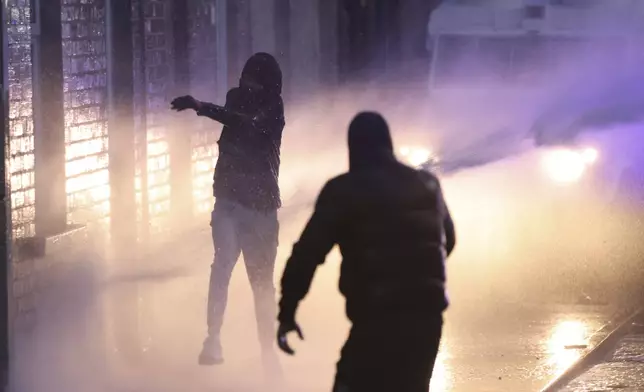 Protesters try to throw items at the police who use water canons to clear them in Ballymena, Northern Ireland, as people protest over an alleged sexual assault in the Co Antrim town, Wednesday, June 11, 2025. (AP Photo/Peter Morrison)