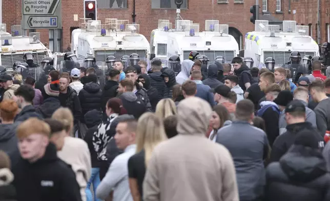 Crowds gather in front of a line of riot police and vans in Ballymena, Northern Ireland, as people protest over an alleged sexual assault in the Co Antrim town, Wednesday, June 11, 2025. (AP Photo/Peter Morrison)