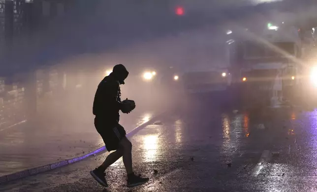 Protesters try to throw items at the police who use water canons to clear them in Ballymena, Northern Ireland, as people protest over an alleged sexual assault in the Co Antrim town, Wednesday, June 11, 2025. (AP Photo/Peter Morrison)