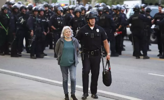 A law enforcement officer escorts a woman out of a protest after she was detained on Wednesday, June 11, 2025, in Los Angeles. (AP Photo/Ethan Swope)