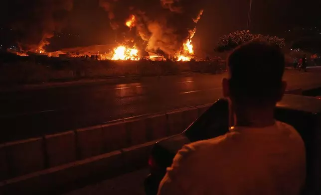 A man looks at flames rising from an oil storage facility after it was hit by an Israeli strike in Tehran, Iran, early Sunday, June 15, 2025. (AP Photo/Vahid Salemi)