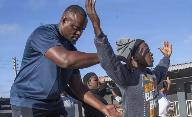 Actions Winya, a yoga instructor assists a man in perfecting his pose in a yoga class at Socialite Bar in Chitungwiza on the outskirts of Harare, Zimbabwe, Friday, June 20, 2025. (AP Photo/Aaron Ufumeli)