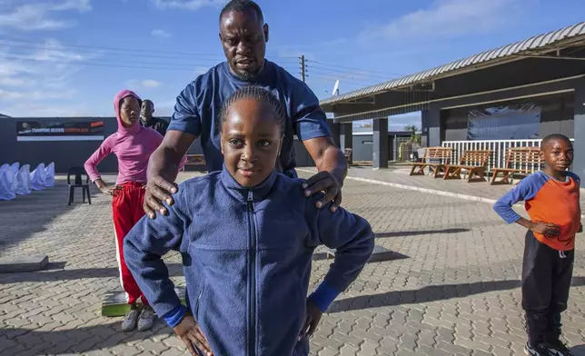 Actions Winya, a yoga instructor assists a young girl in perfecting her pose at Socialite Bar in Chitungwiza on the outskirts of Harare, Zimbabwe, Friday, June 20, 2025. (AP Photo/Aaron Ufumeli)
