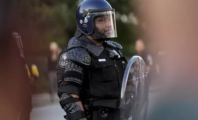 A police officer watches protesters march during an immigration demonstration, Tuesday, June 10, 2025, in Brookhaven, Ga., near Atlanta. (AP Photo/Mike Stewart)