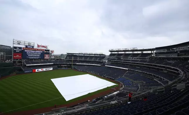 The tarp lies on the field as start of the baseball game between the Washington Nationals and the Texas Rangers is being delayed due to weather, Sunday, June 8, 2025, in Washington. (AP Photo/Nick Wass)