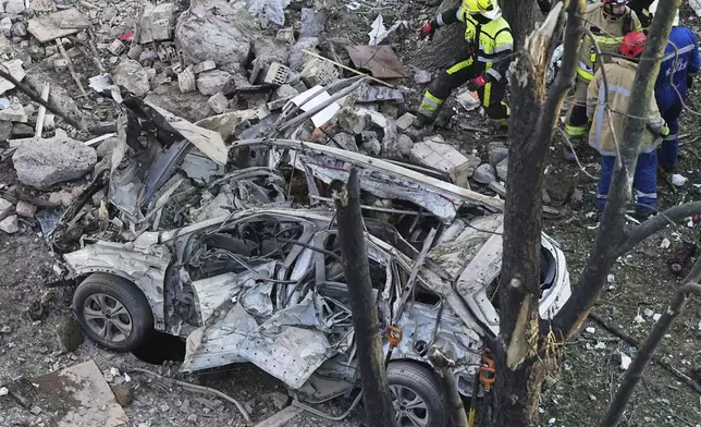 A destroyed car is seen as firefighters work on the site of a damaged building after a Russian attack in Kyiv, Ukraine, early Monday, June 23, 2025. (AP Photo/Efrem Lukatsky)