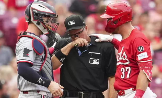 Home plate umpire Tony Randazzo, center, speaks with Cincinnati Reds' Tyler Stephenson (37) and Minnesota Twins' Ryan Jeffers after being hit by a pitch during the second inning of a baseball game, Tuesday, June 17, 2025, in Cincinnati. (AP Photo/Jeff Dean)